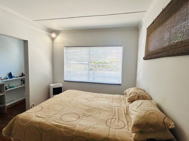 A functional bedroom featuring a window with venetian blinds, cove cornicing, and an adjacent built-in storage or walk-in closet area.