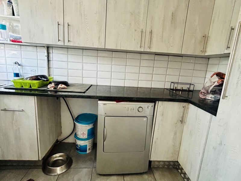 A functional laundry area featuring built-in cabinetry, a tiled backsplash, and durable stone countertops with space for under-counter appliances.