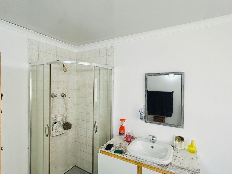A functional bathroom featuring a corner shower enclosure with tiled walls and a vanity unit with a basin and wall-mounted mirror.