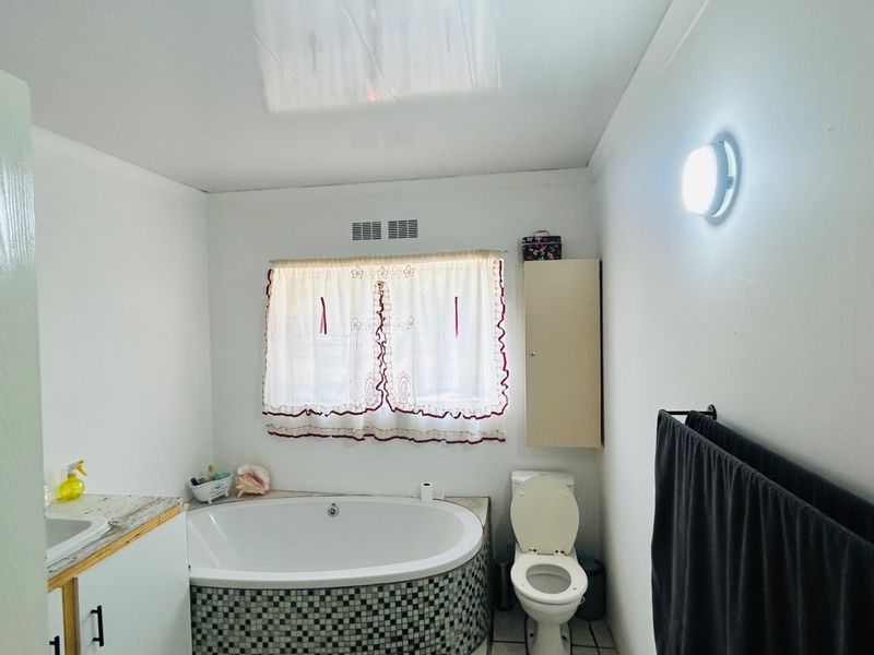 A functional bathroom featuring a built-in corner bathtub with mosaic tiling, a standard toilet, and a vanity sink unit.