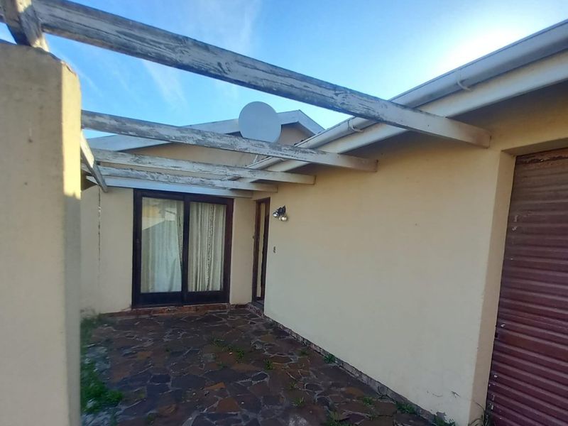 A covered patio area featuring a timber pergola, stone paving, and access to the home via a sliding glass door.