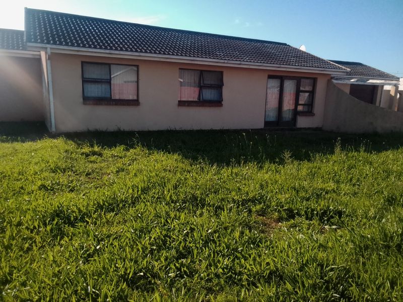 Rear view of a single-story residential house featuring a tiled roof, aluminium window frames, and a sliding glass door, set against an overgrown garden.