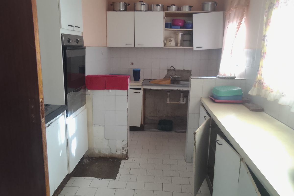 A dated kitchen featuring built-in oven, tiled flooring, and cabinetry. The space requires significant renovation and repair to modernize the finishes and fixtures.