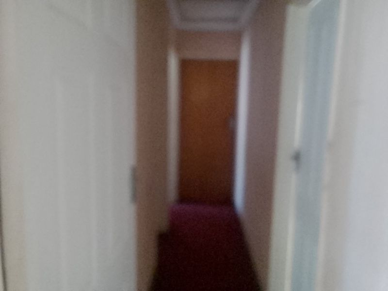 A narrow residential hallway with internal doors, featuring carpeted flooring and plain wall finishes.
