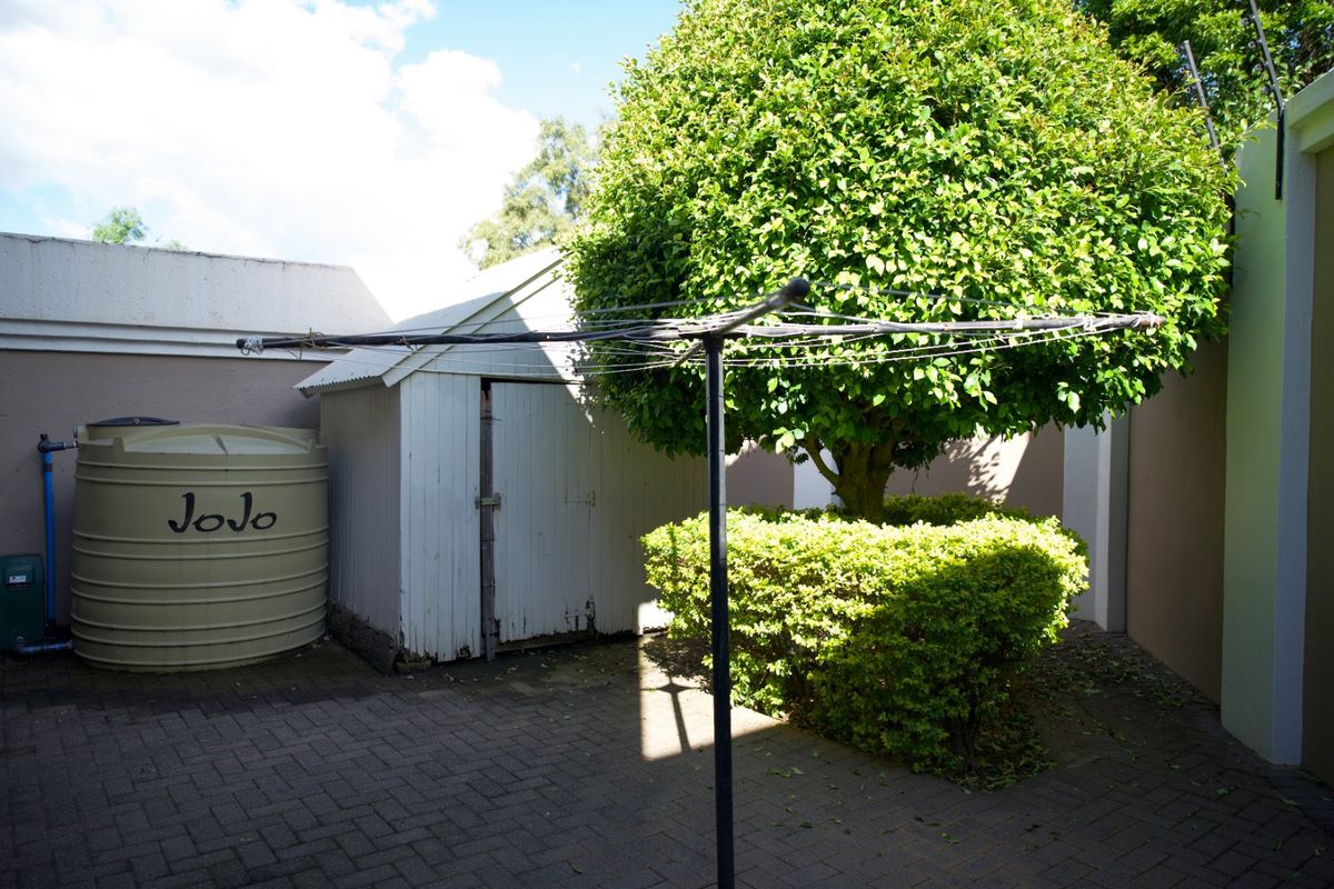 A rear courtyard area featuring a paved surface, a storage shed, and a water storage tank, enclosed by boundary walls.