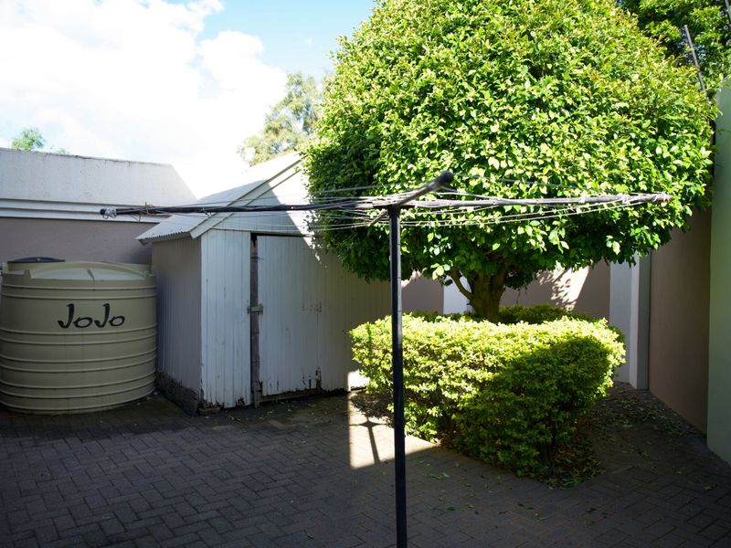 A rear courtyard area featuring a paved surface, a storage shed, and a water storage tank, enclosed by boundary walls.