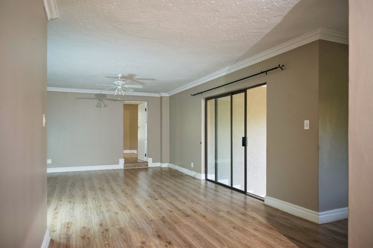 Spacious living area featuring laminate flooring, crown molding, a ceiling fan, and a large sliding glass door providing access to the exterior.