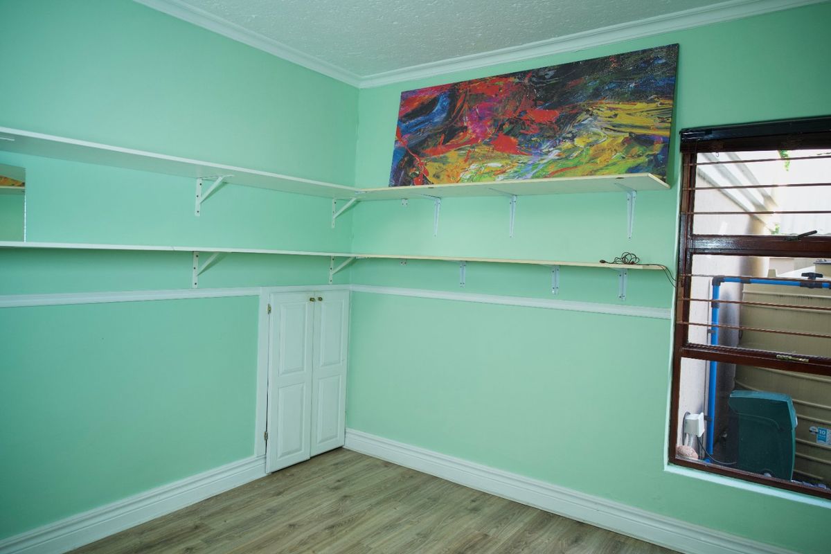 An empty bedroom featuring mint green walls, laminate flooring, built-in shelving units, and a built-in cupboard, providing a versatile space for customization.