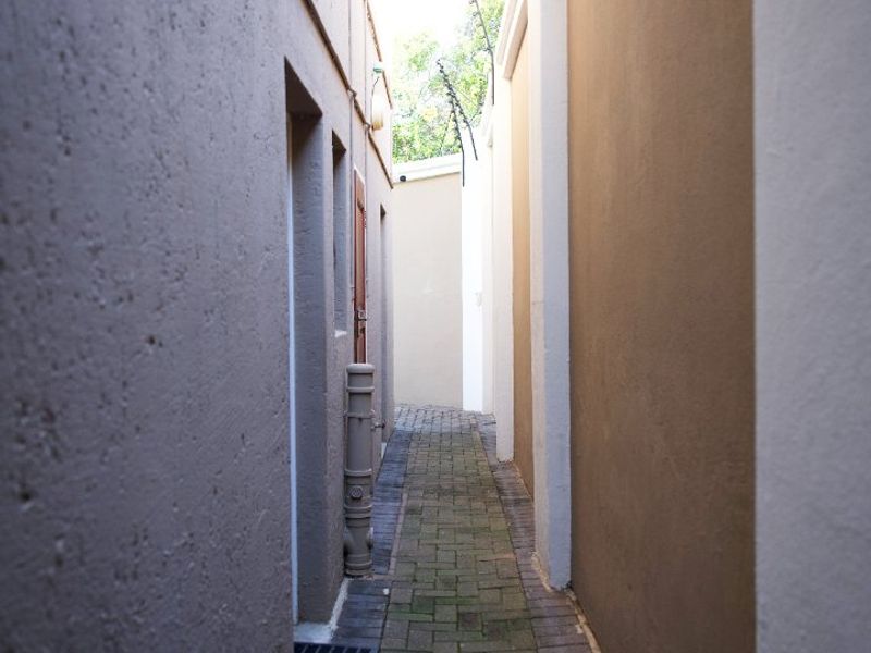 A narrow side passage featuring paved flooring, exterior wall lighting, and security electric fencing along the boundary walls.