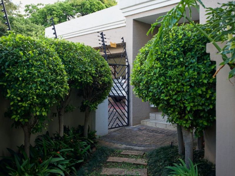 A well-maintained front entrance path featuring a paved walkway, landscaped garden, and secure gated access with electric fencing.