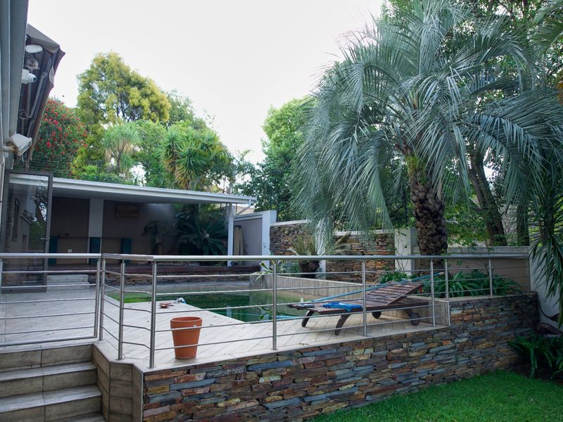 Outdoor pool area featuring a raised tiled deck, stainless steel balustrades, stone-clad retaining walls, and an adjacent covered patio space.