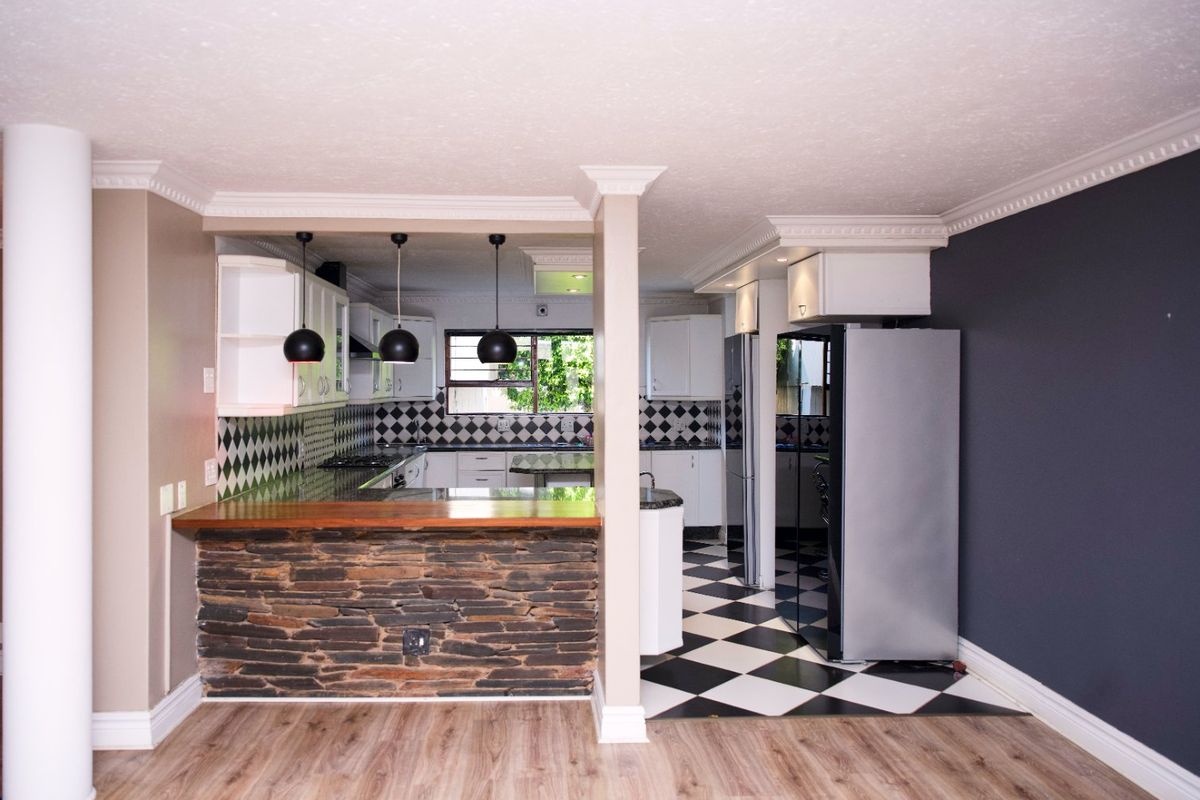 Spacious kitchen featuring a stone-clad breakfast bar, checkered flooring, and ample built-in cabinetry, offering a functional layout with a distinct breakfast counter area.