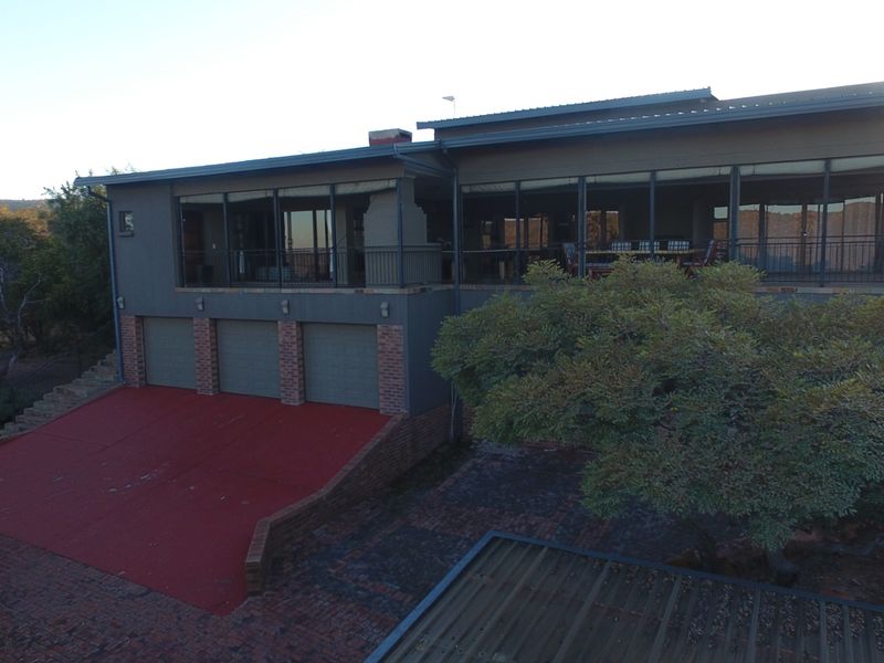 Rear view of a multi-level house featuring a triple garage, a large covered patio area, and a paved driveway.