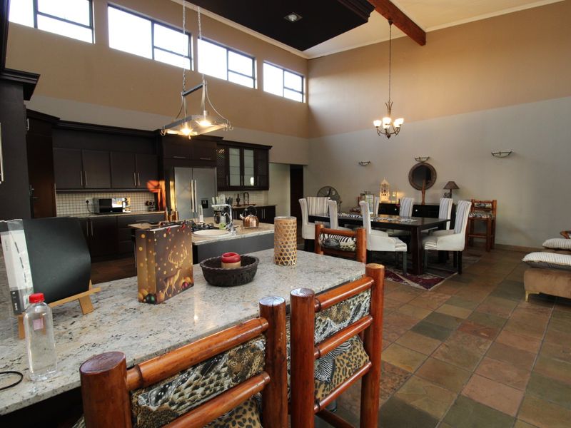 Spacious open-plan kitchen and dining area featuring dark wood cabinetry, granite countertops, slate flooring, and high ceilings with clerestory windows for natural light.