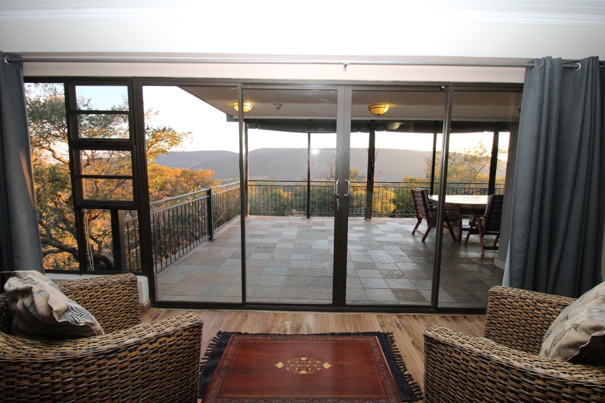 A living room featuring large sliding glass doors that open onto a spacious tiled patio with scenic mountain views.