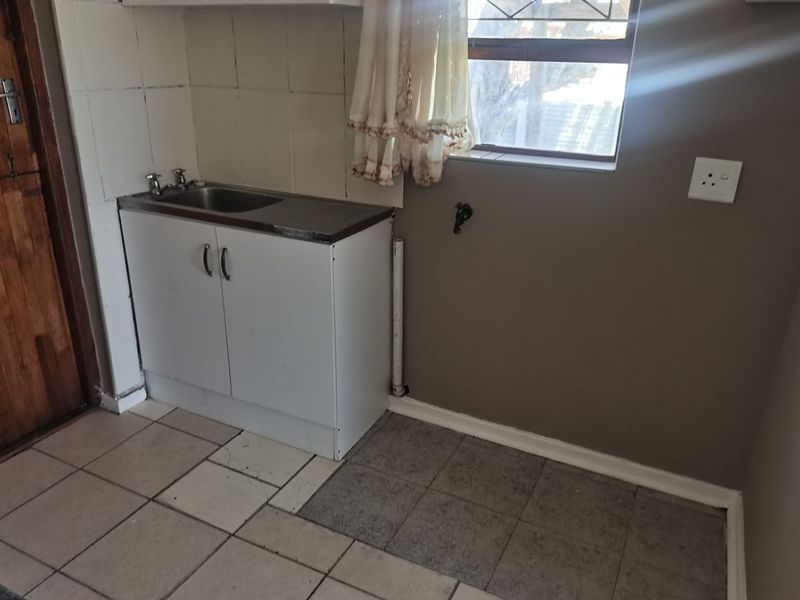 A functional laundry area featuring a built-in sink cabinet, tiled splashback, and dedicated plumbing connections for a washing machine.