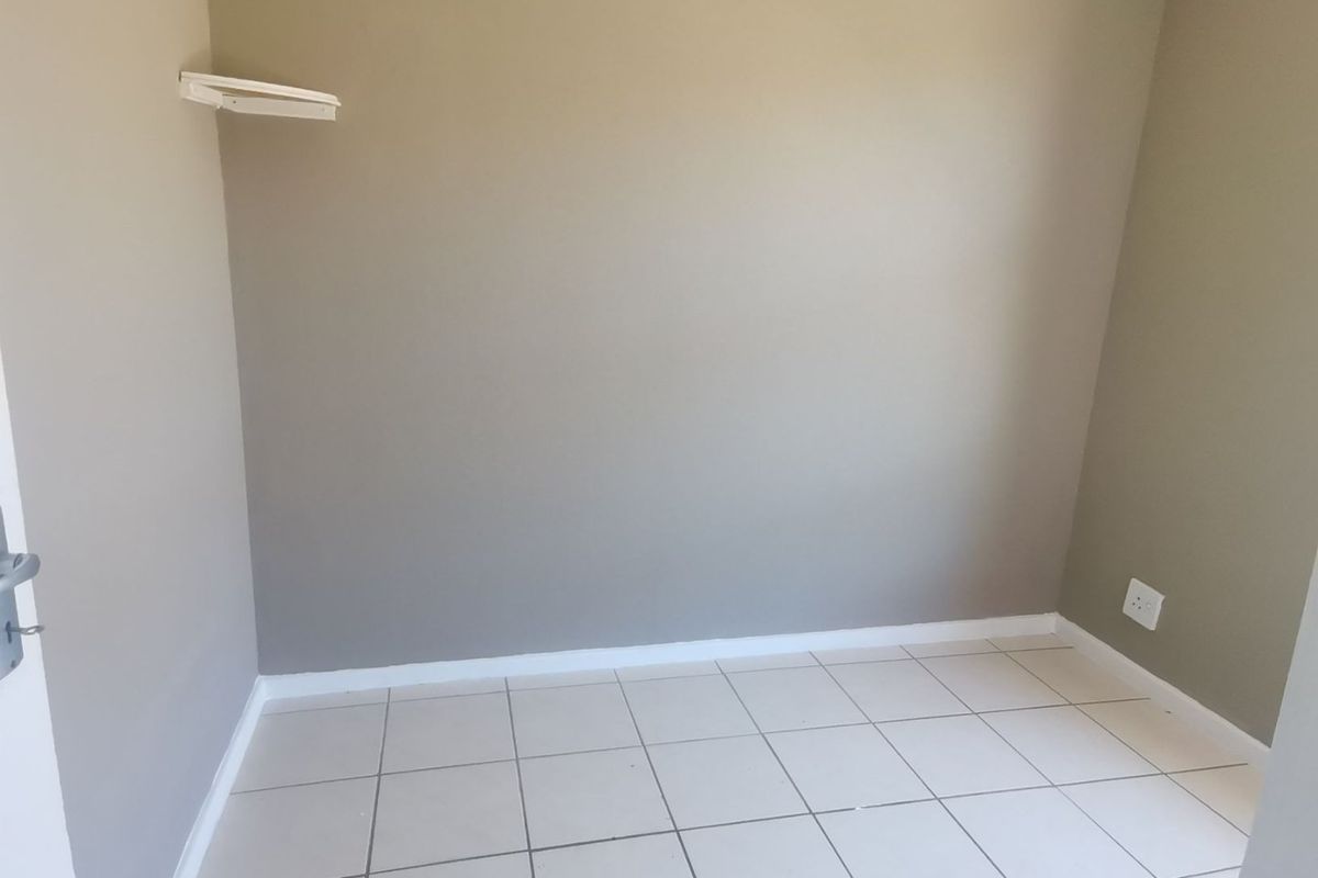 A clean, empty bedroom featuring neutral wall paint, tiled flooring, and a wall-mounted shelf, providing a versatile space ready for personalization.