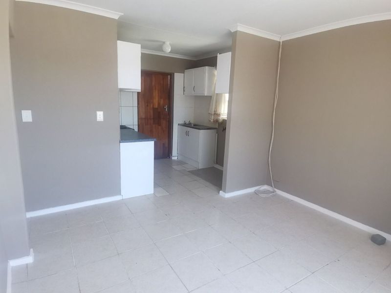 An open-plan living and kitchen area featuring tiled flooring, neutral wall finishes, and basic kitchen cabinetry. The space is vacant and ready for customization.