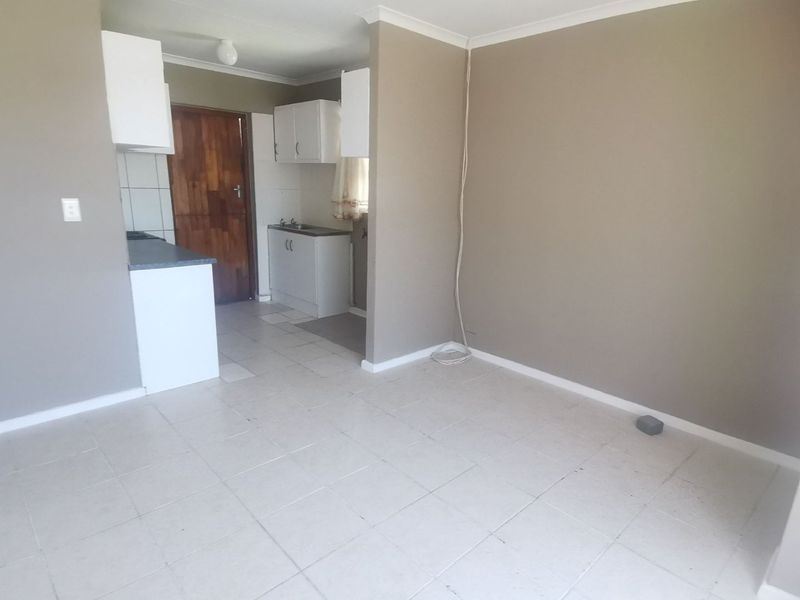 An open-plan living and kitchen area featuring tiled flooring, built-in cabinetry, and a neutral wall finish, currently vacant and ready for renovation.