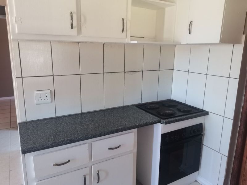 A compact kitchen featuring white cabinetry, a dark laminate countertop, and a built-in electric oven and hob with a tiled splashback.