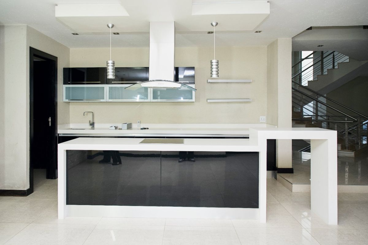 Modern kitchen featuring a sleek black and white island, built-in cabinetry, stainless steel extractor fan, and tiled flooring, adjacent to an open staircase.