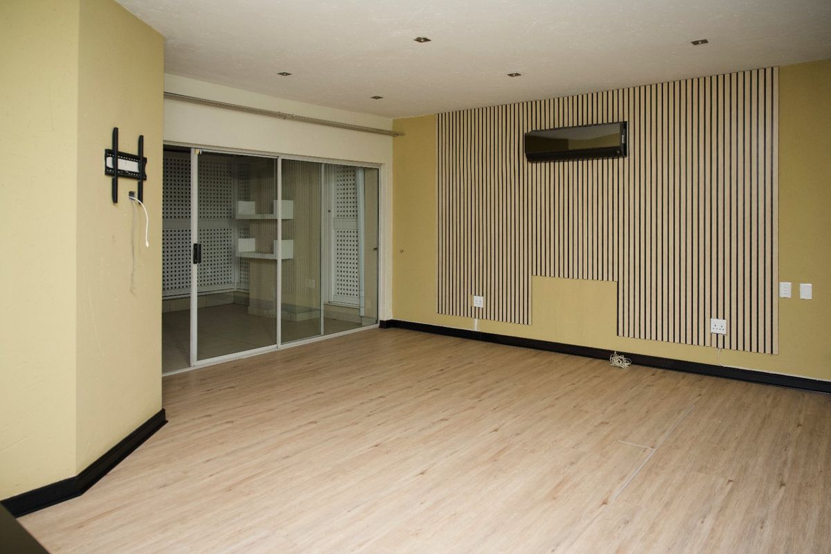 An empty living area featuring modern slatted wood wall paneling, laminate flooring, recessed lighting, and a wall-mounted air conditioning unit.