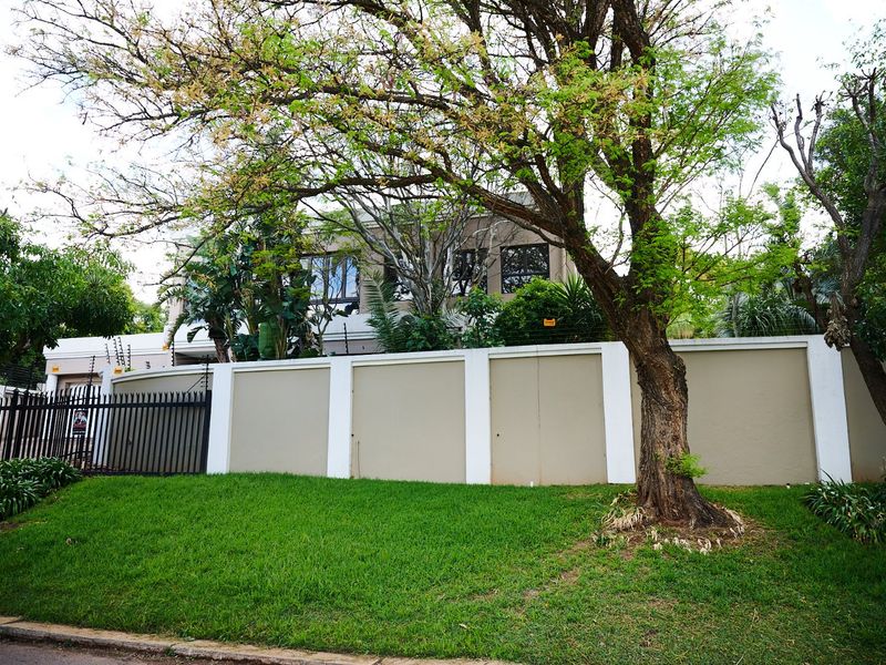 Front view of the property featuring a secure perimeter wall with electric fencing, a metal gate, and a well-maintained lawn.