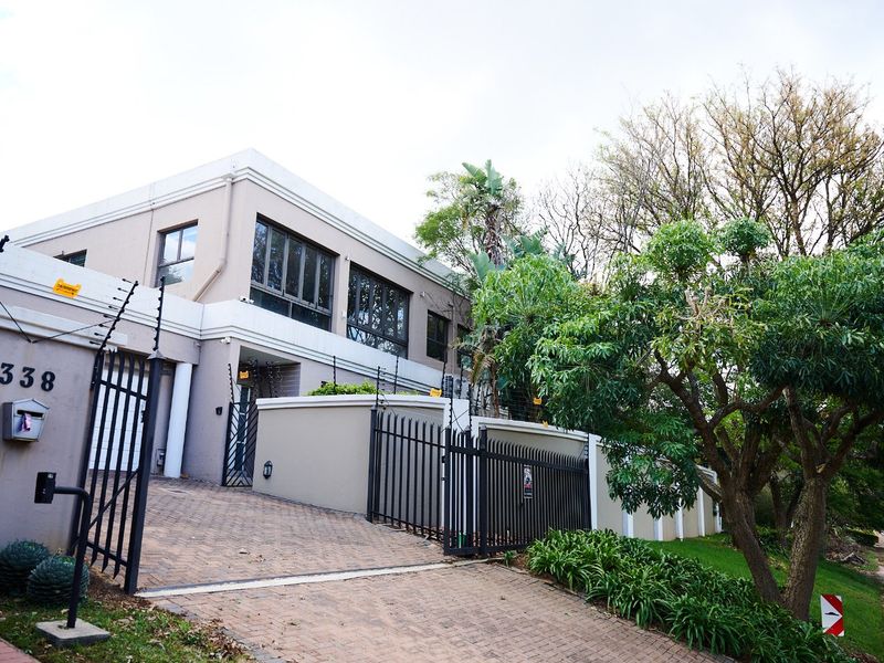 Front elevation of a modern double-story house featuring a paved driveway, secure metal gate, and perimeter electric fencing.
