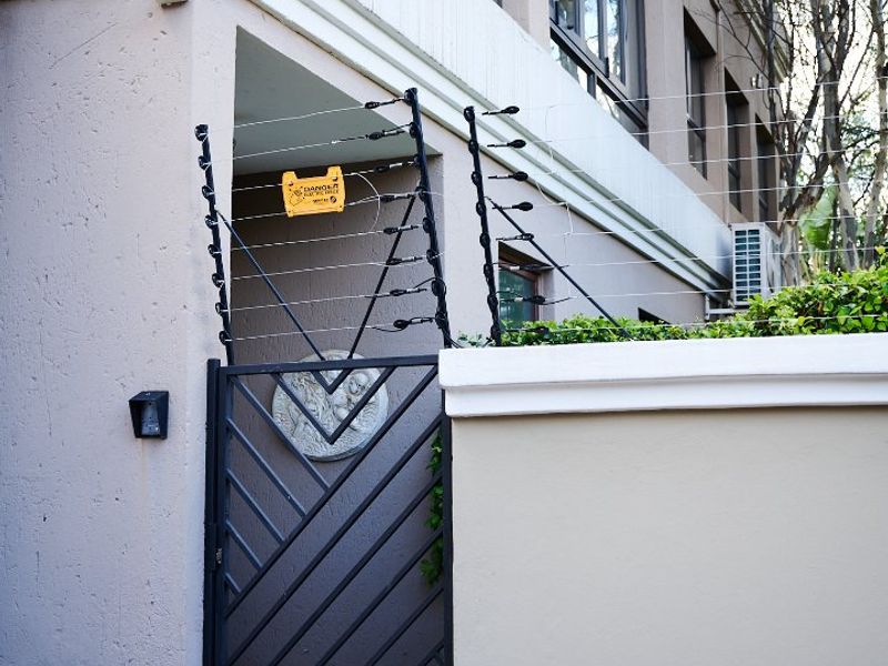 Front entrance area featuring a secure metal gate, electric fencing, and exterior wall-mounted lighting, providing a well-maintained and secure property access point.