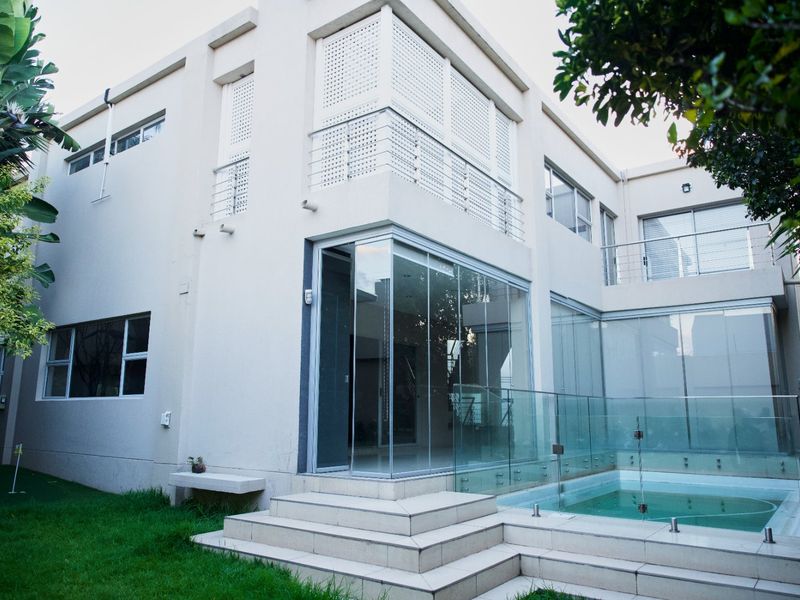 Rear exterior view featuring a modern swimming pool, glass balustrades, tiled patio area, and large sliding glass doors leading into the home.