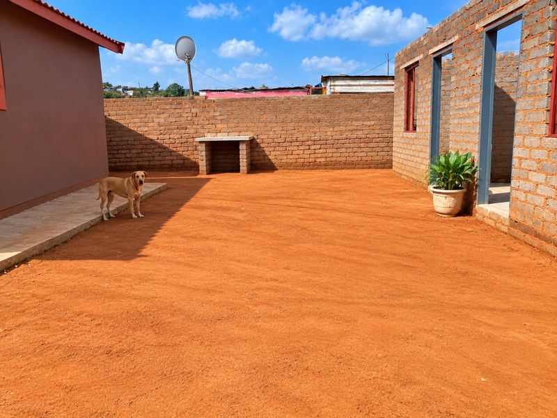 A rear courtyard area featuring a built-in brick braai, perimeter wall, and an adjacent unfinished brick structure, offering potential for landscaping and outdoor development.