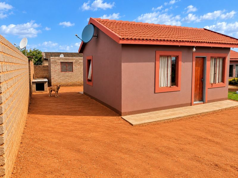 A well-maintained detached house featuring a tiled roof, concrete walkway, and a secure brick boundary wall in the rear yard area.