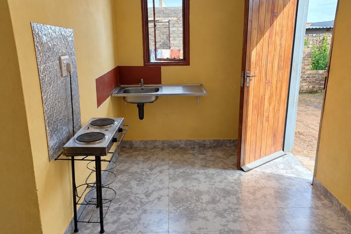 A compact, functional kitchen area featuring tiled flooring, a stainless steel sink, and direct access to the exterior through a timber door.