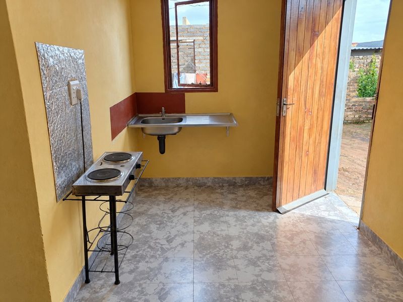 A compact, functional kitchen area featuring tiled flooring, a stainless steel sink, and direct access to the exterior through a timber door.