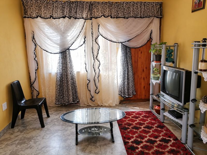 A living room featuring tiled flooring and a wooden door, providing a functional space with natural light filtering through window treatments.