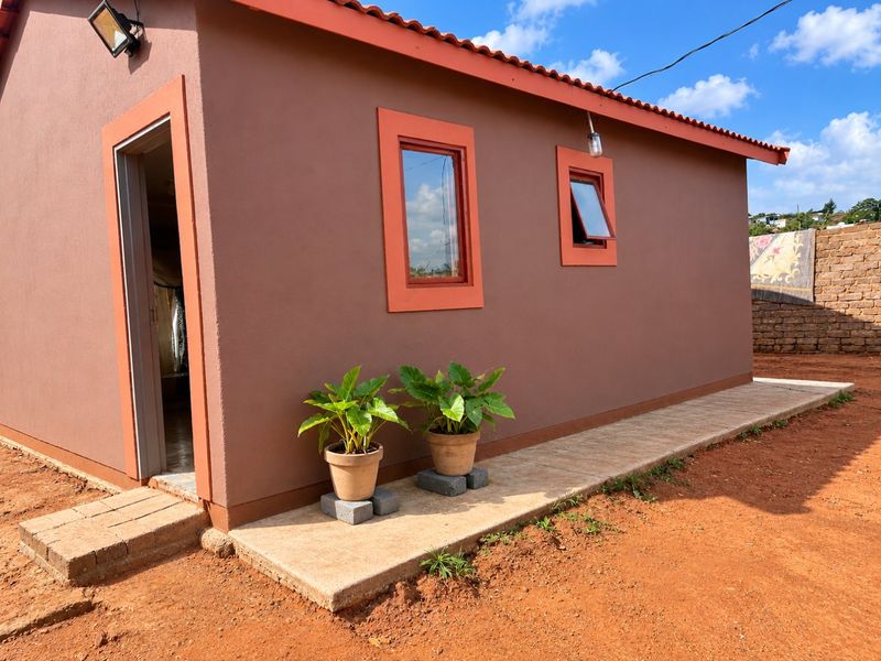 A well-maintained rear exterior view of the house featuring a tiled walkway, terracotta roof tiles, and modern casement windows.