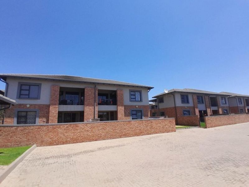 A view of the front exterior of a modern apartment complex featuring brick facades, tiled roofs, and paved driveway access.