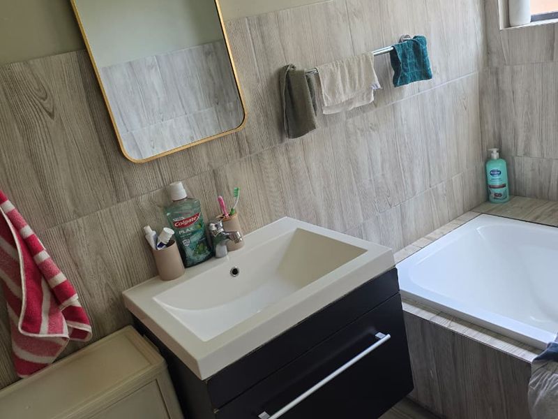 A modern bathroom featuring a wall-mounted vanity with an integrated basin, a built-in bathtub, and wood-look tiling throughout.