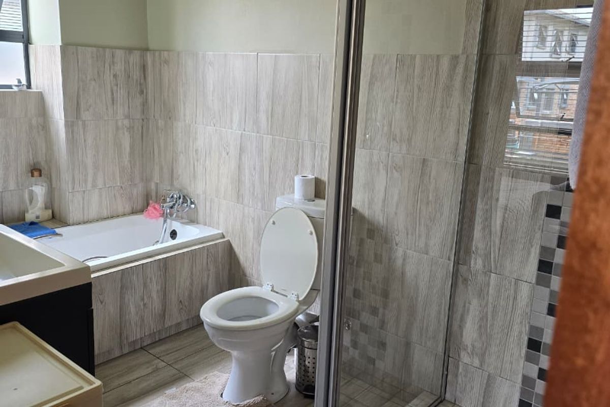A functional bathroom featuring a built-in bathtub, a separate glass-enclosed shower, and modern wood-look wall and floor tiling.