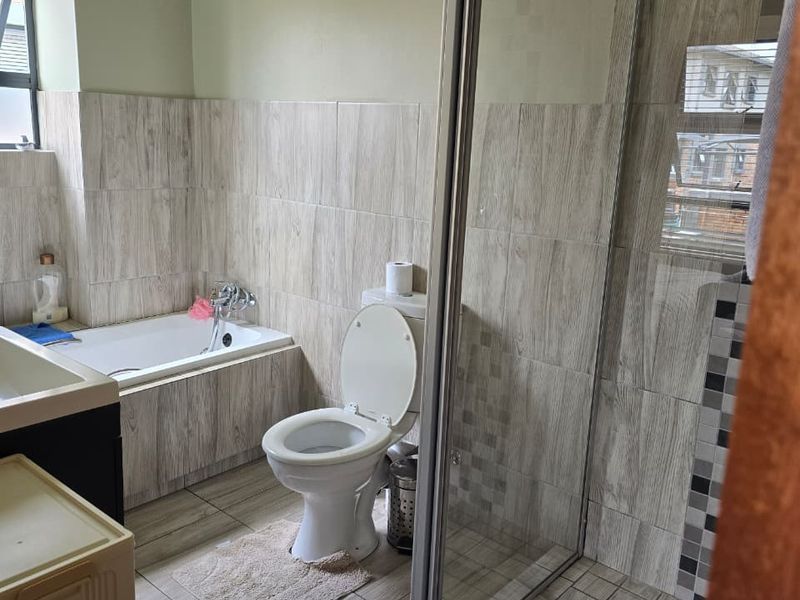 A functional bathroom featuring a built-in bathtub, a separate glass-enclosed shower, and modern wood-look wall and floor tiling.