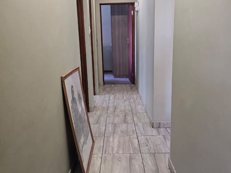 A clean, functional hallway featuring wood-look tiled flooring, neutral wall tones, and access to multiple rooms through traditional wooden door frames.
