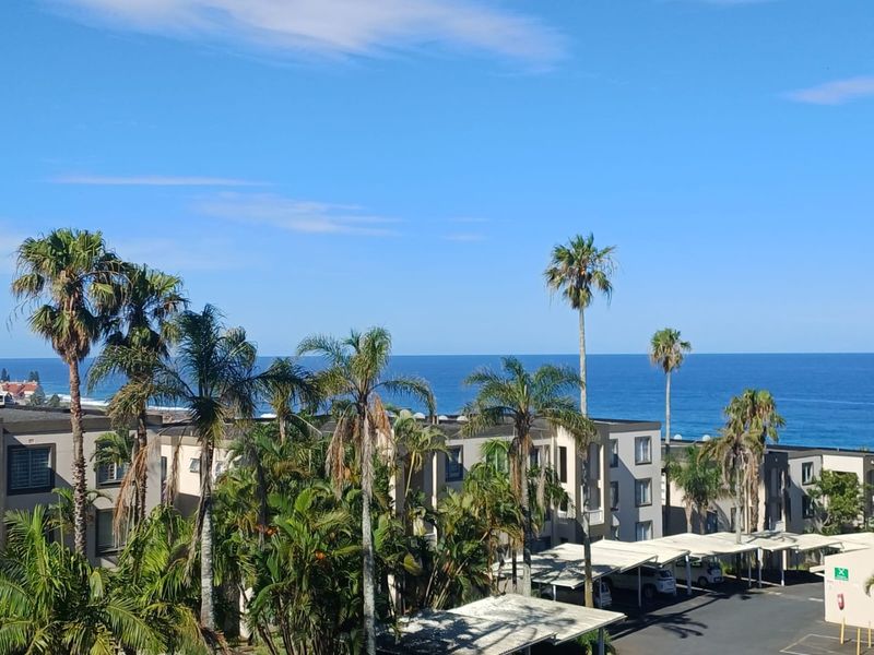 Elevated view overlooking the ocean, lush tropical gardens, and the apartment complex's covered parking area.