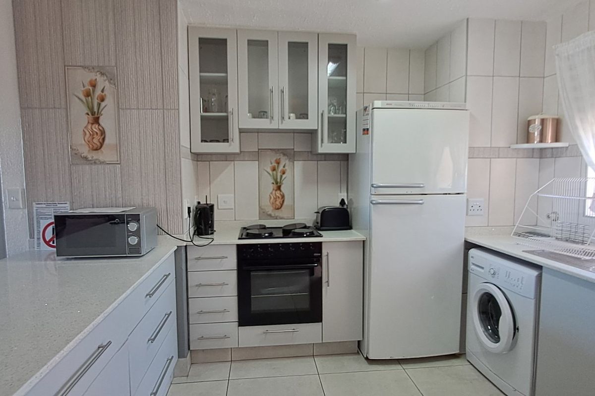 A functional kitchen featuring white cabinetry, stone countertops, built-in oven with gas hob, and tiled finishes, offering a clean and practical workspace.