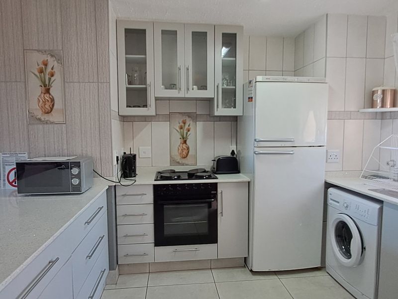 A functional kitchen featuring white cabinetry, stone countertops, built-in oven with gas hob, and tiled finishes, offering a clean and practical workspace.