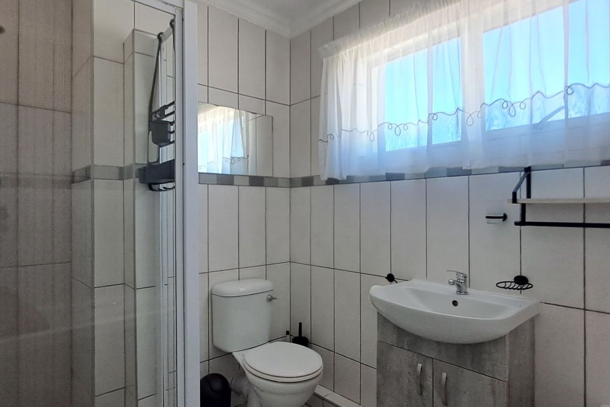 A functional bathroom featuring a shower enclosure, a vanity basin with storage cabinet, and a toilet, finished with neutral wall and floor tiling.