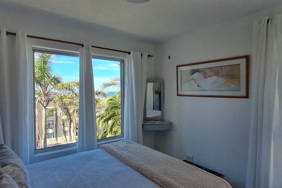 A bright bedroom featuring large windows with scenic views, a built-in corner vanity shelf, and neutral finishes.