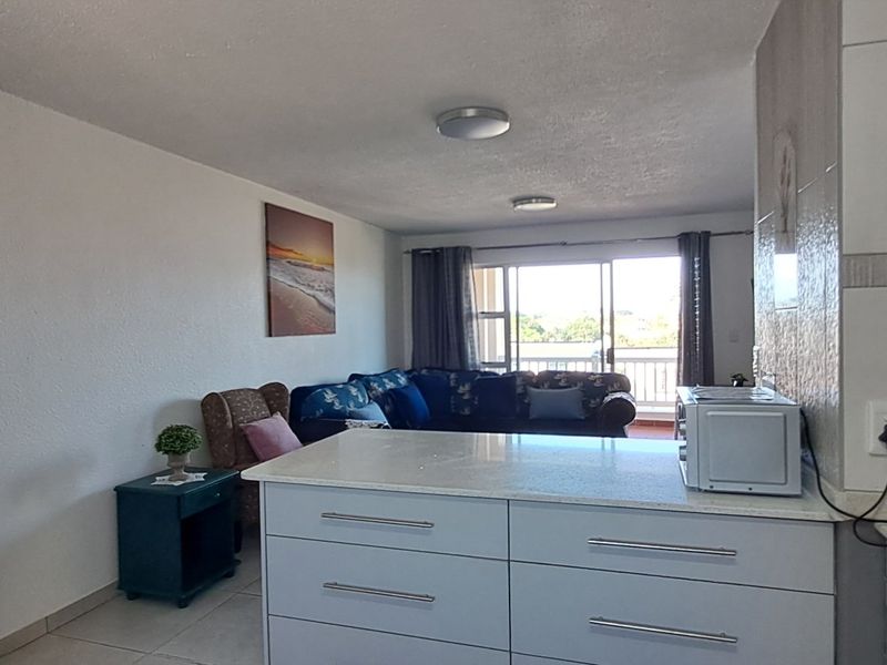 Open plan living area featuring a kitchen island with cabinetry, tiled floors, and a sliding door leading to an outdoor balcony.
