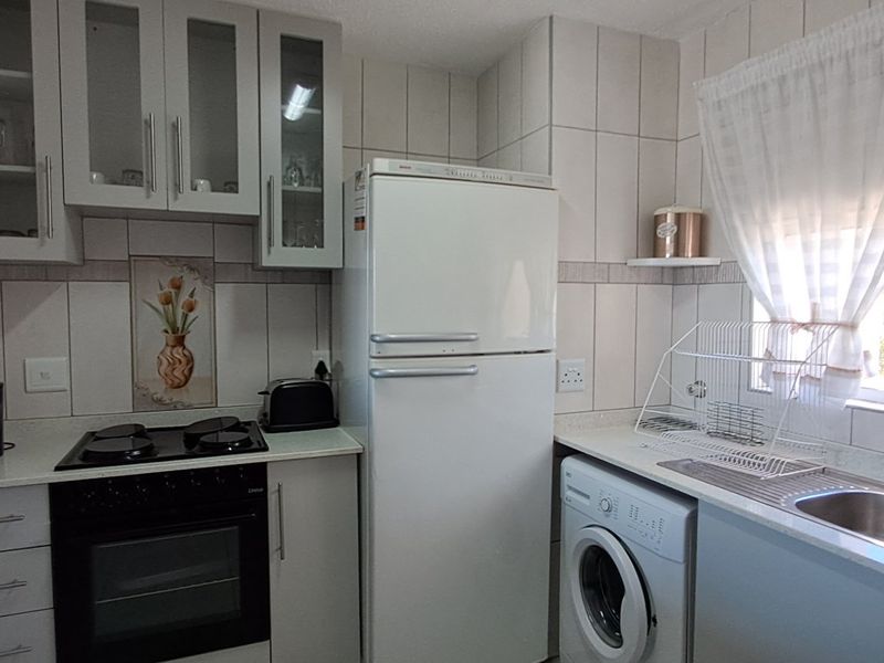 A functional kitchen featuring built-in cabinetry, an electric hob, an oven, and a double sink with integrated laundry plumbing.