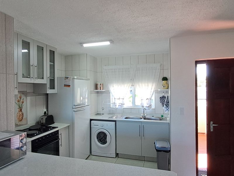 Functional kitchen featuring built-in cabinetry, integrated oven and hob, double sink, and dedicated laundry plumbing space.