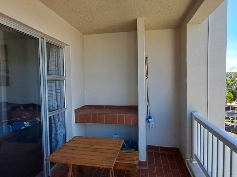 Covered balcony featuring a built-in brick braai, tiled flooring, and a metal balustrade, offering views of the surrounding complex grounds.